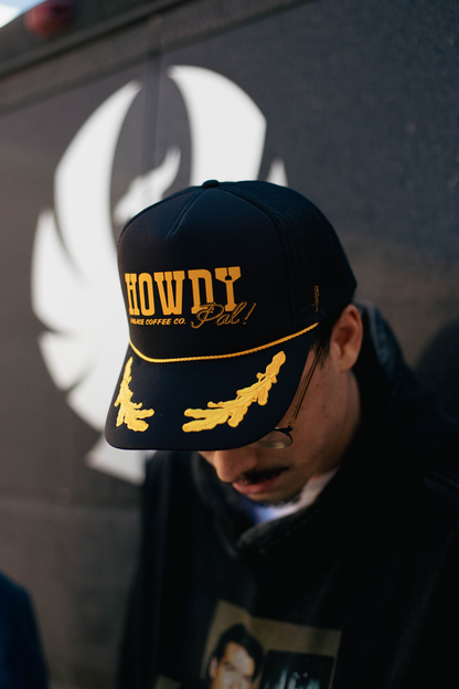 Person wearing a black cap with yellow text and graphics against a dark background